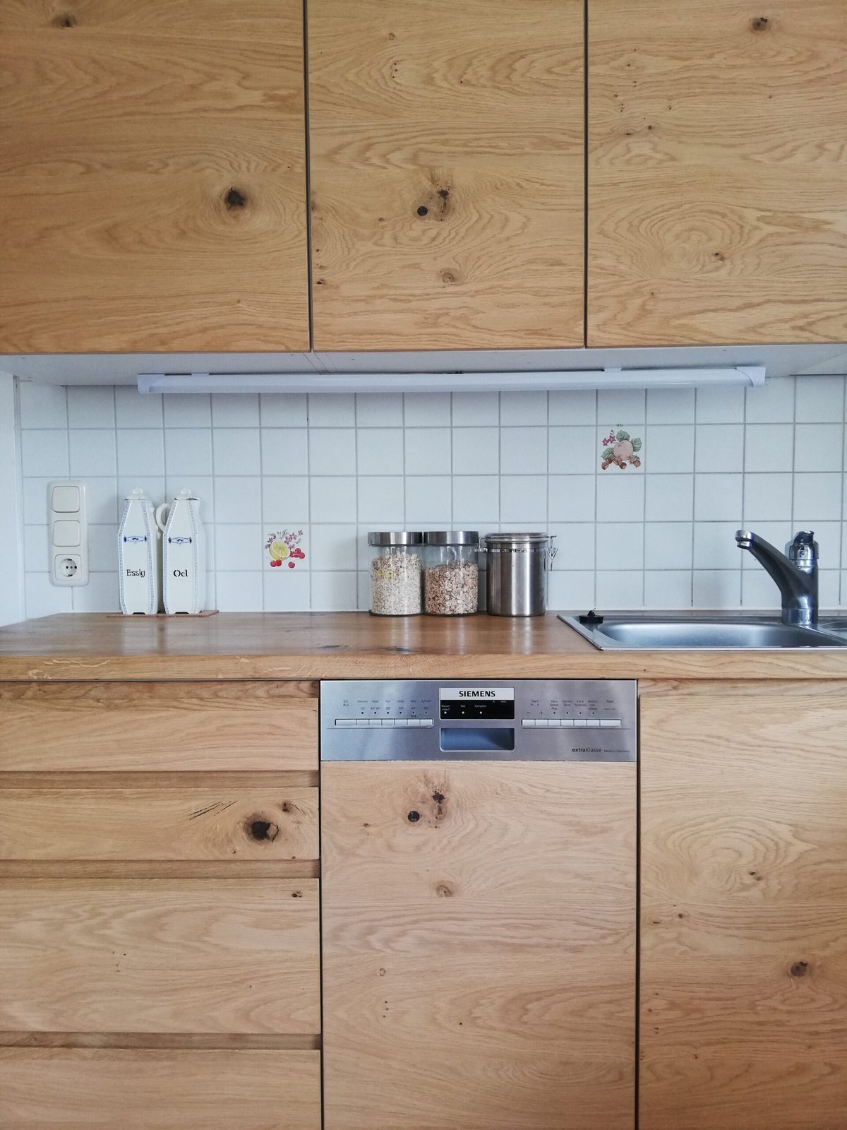 Küchenzeile mit astreichen Holzfronten und Arbeitsplatte aus Holz vor weißen Fliesen