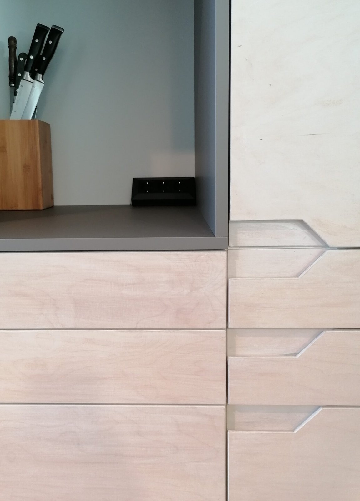 Küchenschränke mit hellen Schubladen und eingelassenen Griffmulden neben einem grauen Schrank